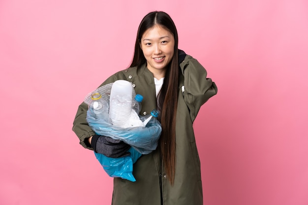 Chinese girl holding a bag full of plastic bottles to recycle over isolated pink wall laughing