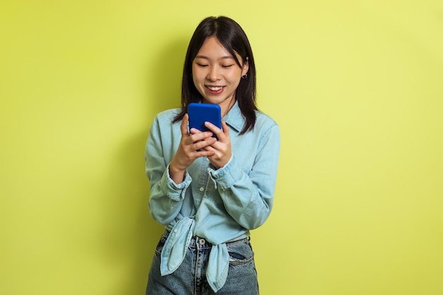 黄色の背景にポーズをとって携帯電話のテキスト メッセージを使用して中国の女性
