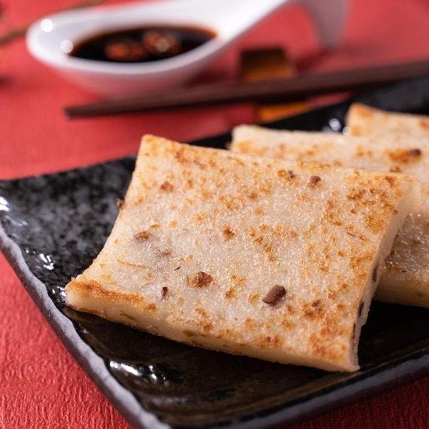 Chinese lunar new year food concept Delicious turnip radish cake local cuisine in restaurant with soy sauce on red background close up copy space