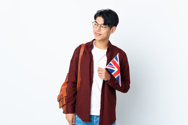 Chinese man holding an UK flag isolated on purple space looking to the side and smiling