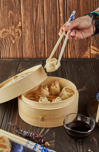 Chinese meat dumplings steamed in a bamboo steamer and a hand picking one up with chopsticks