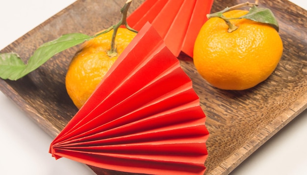 Китайский Новый год, композиция с мандаринами, забавные оригами из красной бумаги на темной деревянной тарелке на белом фоне.