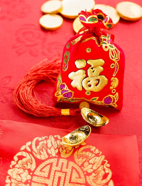 Chinese new year decoration: red felt fabric packet or ang pow with word "prosperous" and golden ingots on red fabric