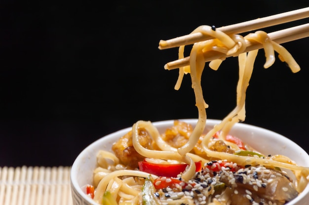 Foto i noodles cinesi sono tenuti con bastoncini di bambù