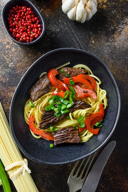 Chinese noodles with vegetables and beef in black bowl