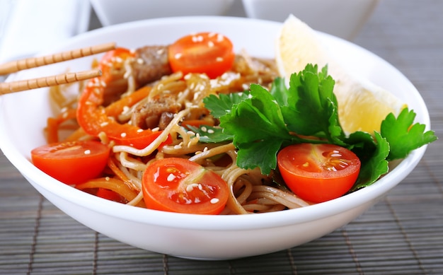 Photo chinese noodles with vegetables and roasted meat in bowl on napkin, on wooden space