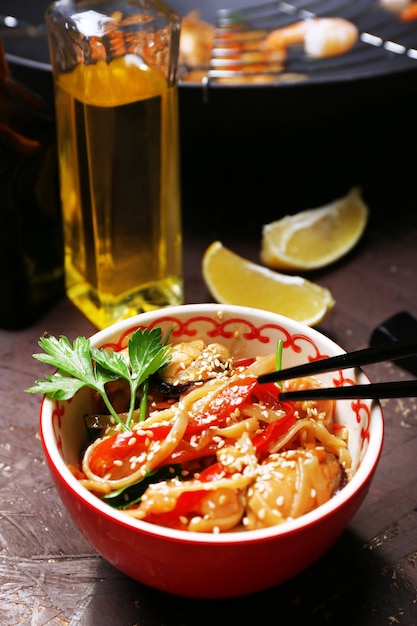 Photo chinese noodles with vegetables and seafood in bowl and wok on wooden background