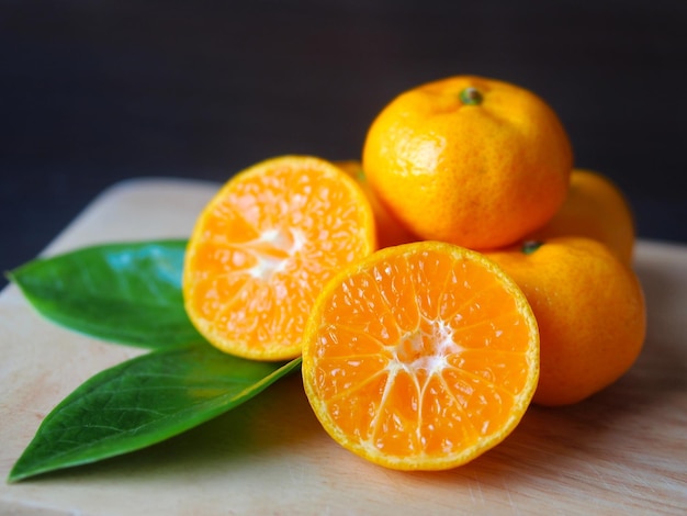 Chinese orange fruit cut in half with green leafs on a wooden cutting board