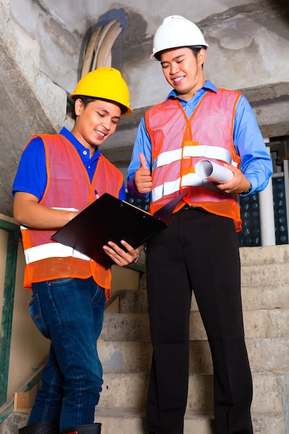 Chinese supervisor or controller and worker or architect look on building site on a clipboard