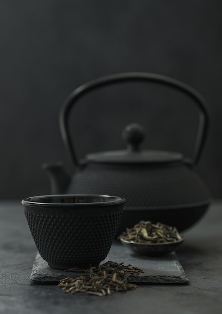 Chinese teapot with plate of loose black tea and cup on black background