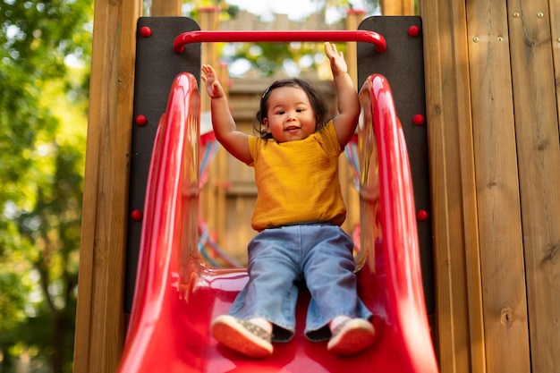 Chinese toddler infant girl enjoying playground fun riding slide outdoors