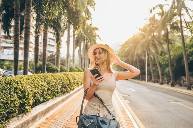 Turista cinese che cammina nelle vie della città sul turismo di vacanza dell'asia. bella donna caucasica con lo zaino, smartphone. concetto di lifestyle di viaggio. strada con palme verdi e autostrada a sanya, hainan.