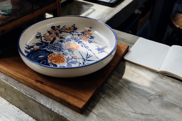 Chinese traditional decorative ceramic plate on wooden block with open notebook on kitchen counter.