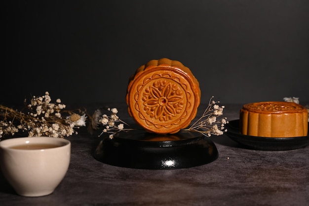 Chinese traditional mid autumn festival moon cake with cup of tea and dried flowers on black stone table