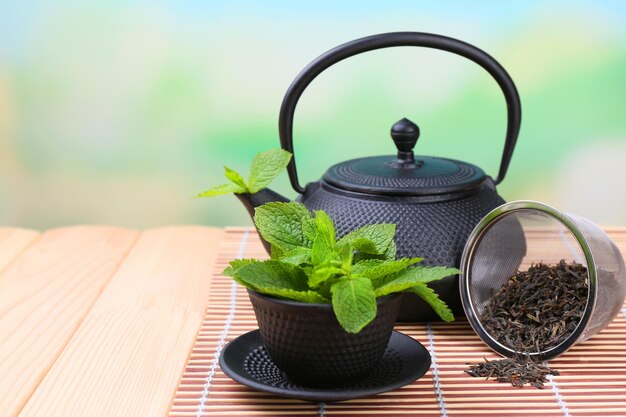 Chinese traditional teapot with fresh mint leaves on wooden table on bright background