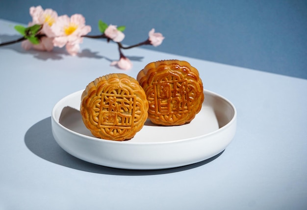 Chinese traditionele gebak Maancake, Mooncake met roze bloemen, voor Mid-Autumn Festival, hard zonlicht, blauwe achtergrond, modern stilleven