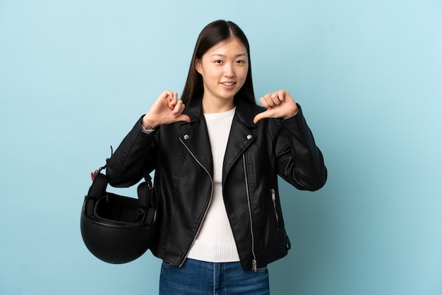 Chinese vrouw die een motorfietshelm over geïsoleerde blauwe trots en zelfverzekerde muur houdt