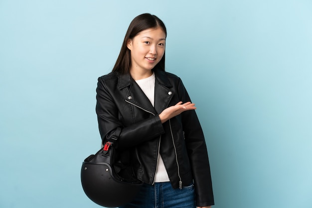 Chinese woman holding a motorcycle helmet over isolated blue wall extending hands to the side for inviting to come