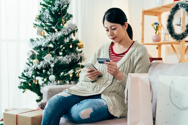 クレジット カードでクリスマス ギフト ショッピングのオンライン決済を行う中国人女性。スマートフォンでカード情報を入力するきれいな女性。テクノロジーとライフスタイル。ボクシングデーの販売コンセプト