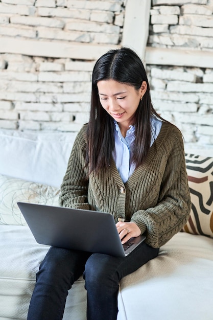 Chinese woman uses laptop on sofa blending work and comfort