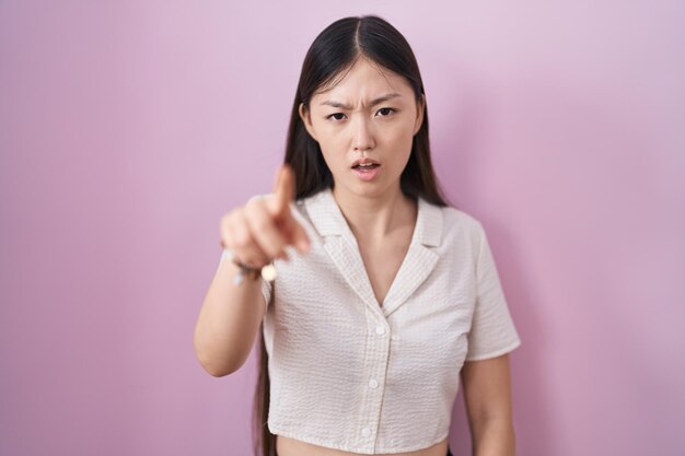 사진 분홍색 배경 위에 서 있는 중국 젊은 여성은 당신에게 화가 나고 분노한 카메라를 향해 불쾌하고 좌절감을 나타냈습니다.