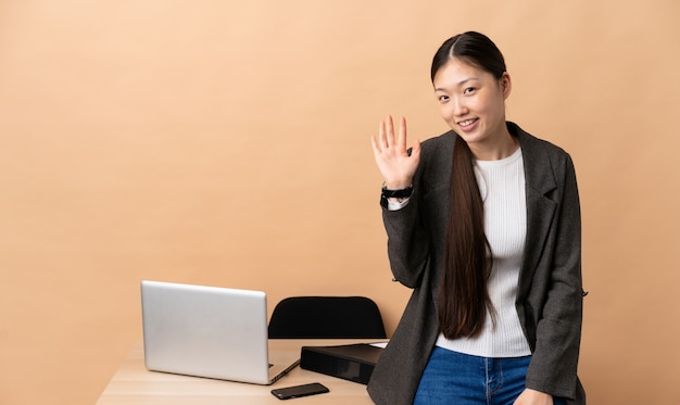 Chinese zakenvrouw in haar werkplek groeten met hand met gelukkige uitdrukking