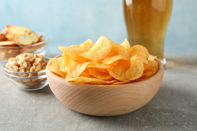 Foto chips in een kom en een glas bier. biersnacks, biernoten op grijze lijst tegen blauw, ruimte voor tekst. detailopname