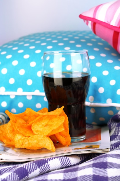 Chips in kom cola en TV-afstandsbediening op plaid op kussens achtergrond