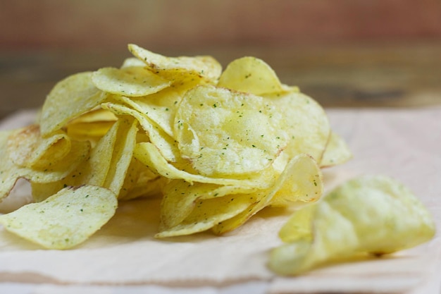 Chips lie on paper on a wooden table. Fast food