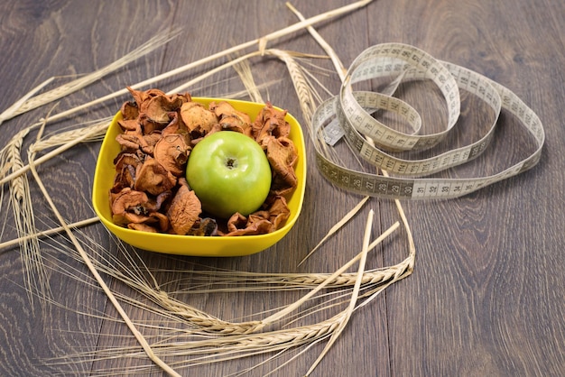 Chips made from apples in yellow plate with green apple and wheat spica around on wooden table top view copy space