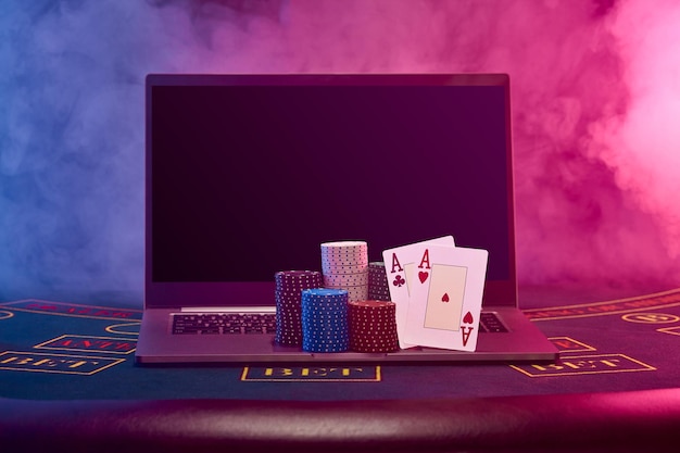 Chips piles and two aces on laptop standing on blue cover of playing table black smoke background po