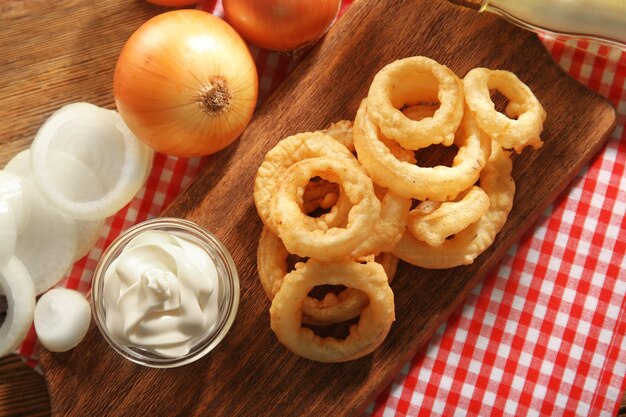 Anelli di patatine fritte con salsa e cipolla sul primo piano del tagliere