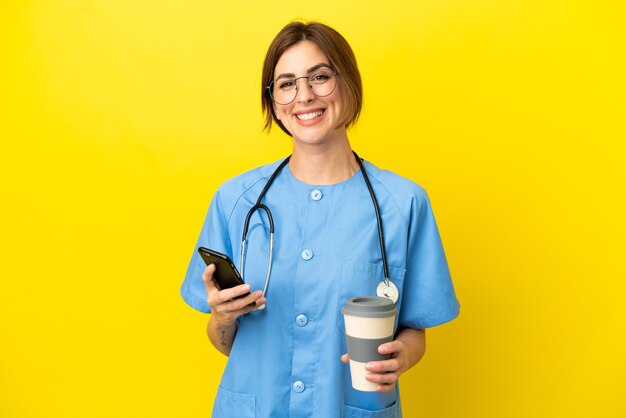 Chirurg arts vrouw geïsoleerd op gele achtergrond met koffie om mee te nemen en een mobiel