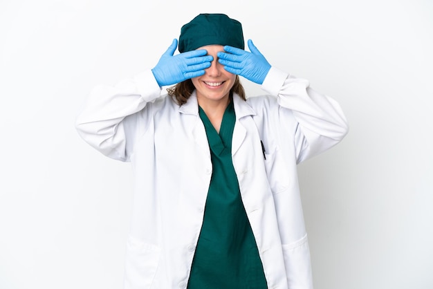 Chirurg blanke vrouw in groen uniform geïsoleerd op een witte achtergrond die ogen bedekt door handen