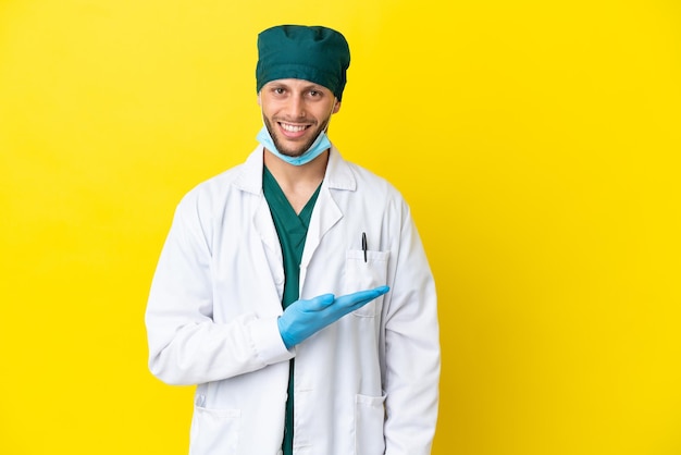 Chirurg blonde man in groen uniform geïsoleerd op gele achtergrond die een idee presenteert terwijl hij glimlacht naar