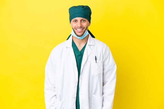 Chirurg blonde man in groen uniform geïsoleerd op gele achtergrond lachen