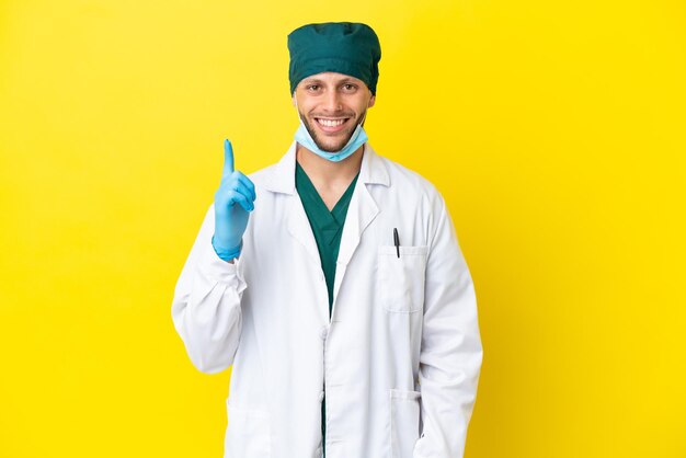 Chirurg blonde man in groen uniform geïsoleerd op gele achtergrond wijzend met de wijsvinger een geweldig idee