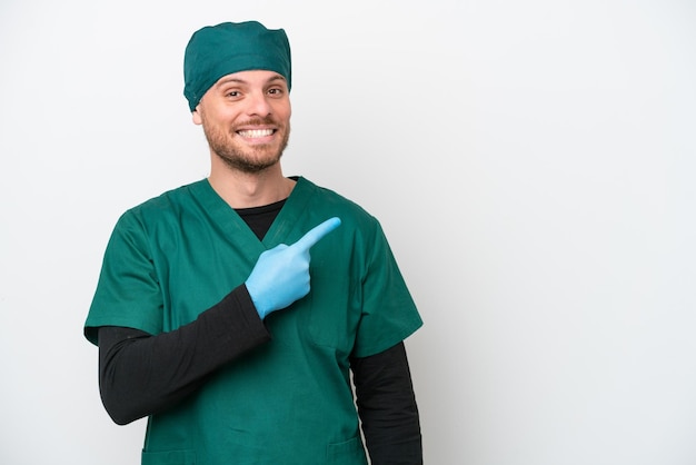 Chirurg braziliaanse man in groen uniform geïsoleerd op een witte achtergrond, wijzend naar de zijkant om een product te presenteren