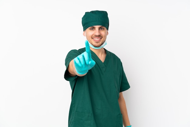 Chirurg in groene uniform geïsoleerd op geïsoleerde witte muur tonen en een vinger opheffen