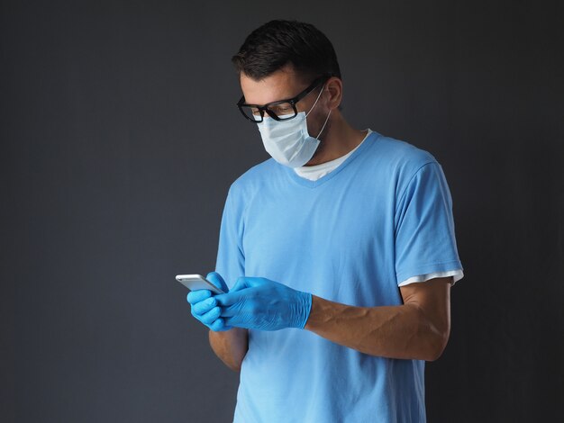 Chirurg in medisch masker en handschoenen die op celtelefoon texting.