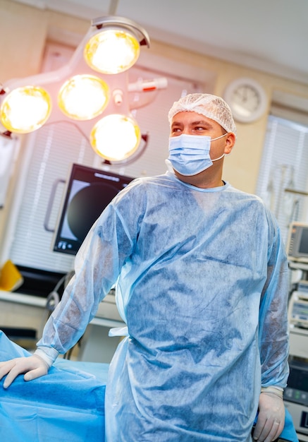 Chirurg in scrubs en gezichtsmasker die in de operatiekamer staat en wegkijkt Portret van mannelijke arts in moderne medische kamer