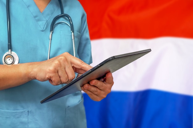 Chirurg of arts met behulp van een digitale tablet op de achtergrond van de Nederlandse vlag