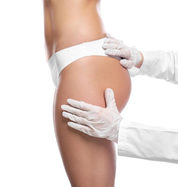 Chirurg onderzoekt vrouwelijk lichaam voor een plastische operatie op een witte achtergrond