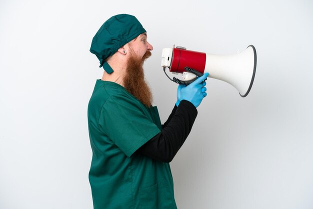 Chirurg roodharige man in groen uniform geïsoleerd op een witte achtergrond schreeuwen door een megafoon