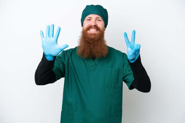 Chirurg roodharige man in groen uniform geïsoleerd op een witte achtergrond tellen zeven met vingers