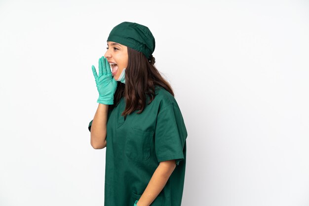 Chirurg vrouw in groen uniform geïsoleerd op witte muur schreeuwen met mond wijd open voor de zijkant