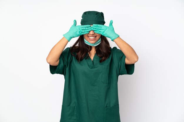 Chirurgenvrouw in groen uniform geïsoleerd op witte muur die ogen behandelen door handen