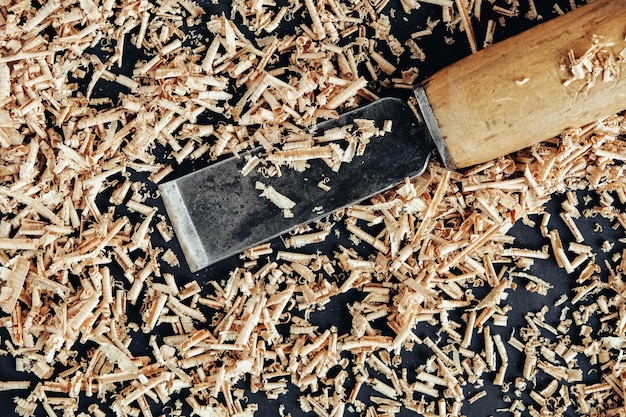 Chisel with wooden shavings on black background. Old woodworking hand tool. Top view. Copy, empty space for text