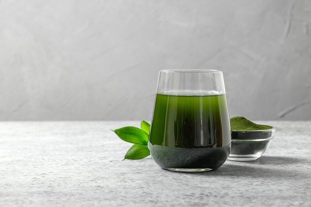 Chlorella gezonde detoxdrank in glas en poeder in kom op een grijze ruimte