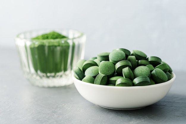 Chlorella of spirulina in de vorm van tabletten en poeder op een grijze betonnen achtergrond.